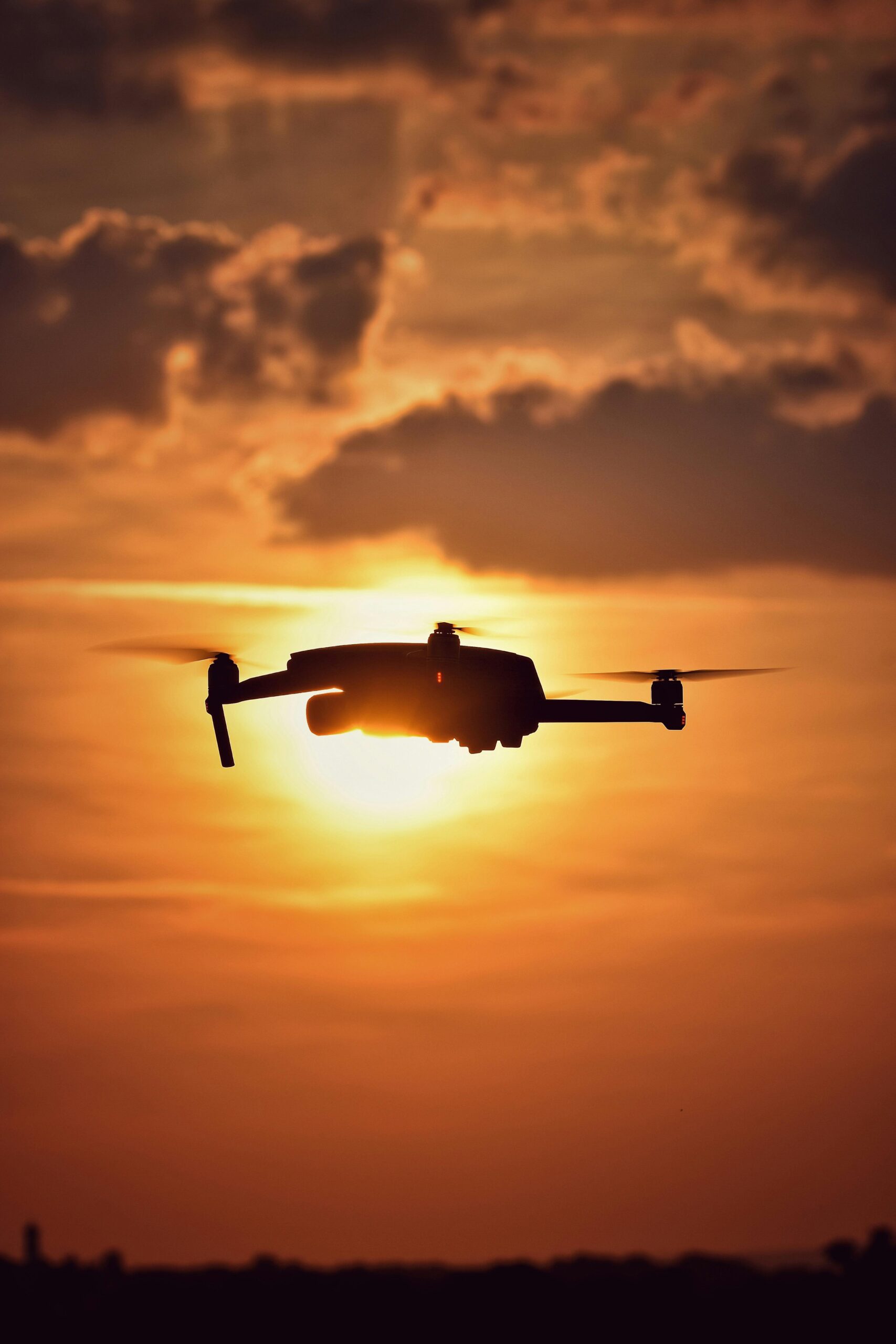A drone's silhouette soaring through a dramatic, vibrant sunset sky with scattered clouds.
