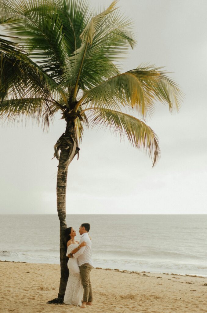 A couple embracing near a palm tree on a tropical beach, perfect for prewedding romance.